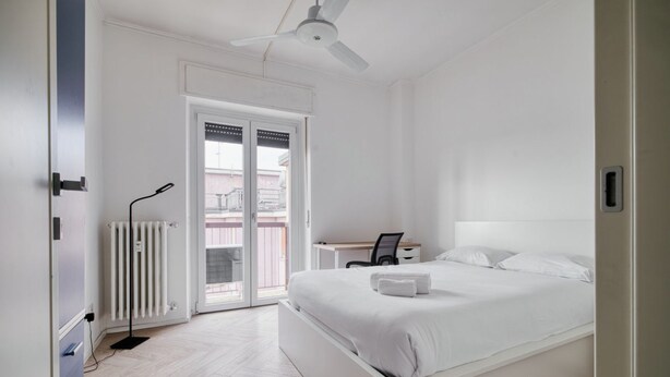 Una camera da letto con un letto, una scrivania, una sedia, un termosifone e una ventola a soffitto.