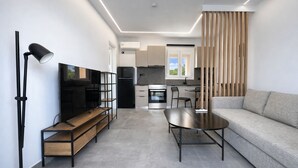 A modern living room with a flat-screen TV, a sofa, a coffee table, and a dining area with a table and chairs.