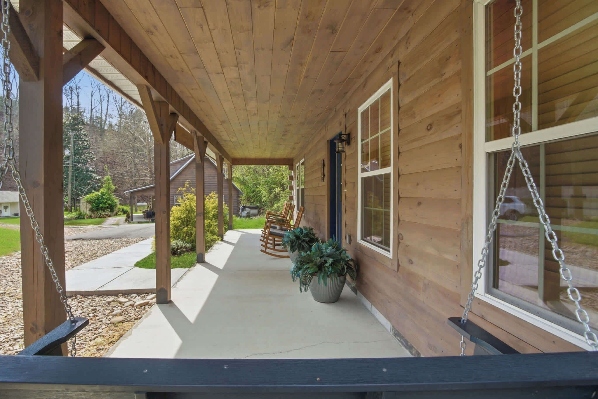 A wooden porch with a swing, potted plants, and a view of the street.