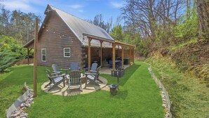 Une cabane en rondins dotée d’un patio couvert, de meubles d’extérieur et d’une pelouse bien entretenue.
