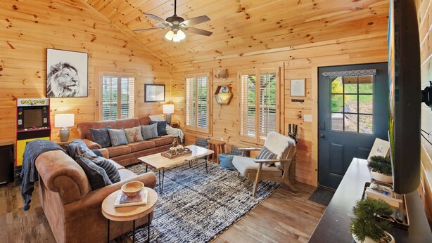 L’intérieur d’un chalet accueillant, avec un plafond en bois, un canapé, une table basse, un fauteuil et un téléviseur.