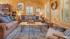L’intérieur chaleureux d’un chalet avec un plafond en bois, un canapé, une table basse et un coin cuisine équipé d’un four à micro-ondes.