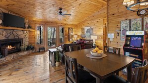 A log cabin interior with a stone fireplace, wooden dining table, and Pac-Man arcade. - Heart's Hideaway - Blue Ridge, GA (Morganton)