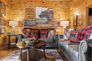 A cabin interior with a wooden interior, a sofa set, a round coffee table, and decorative pillows. - Heart's Hideaway - Blue Ridge, GA (Morganton)