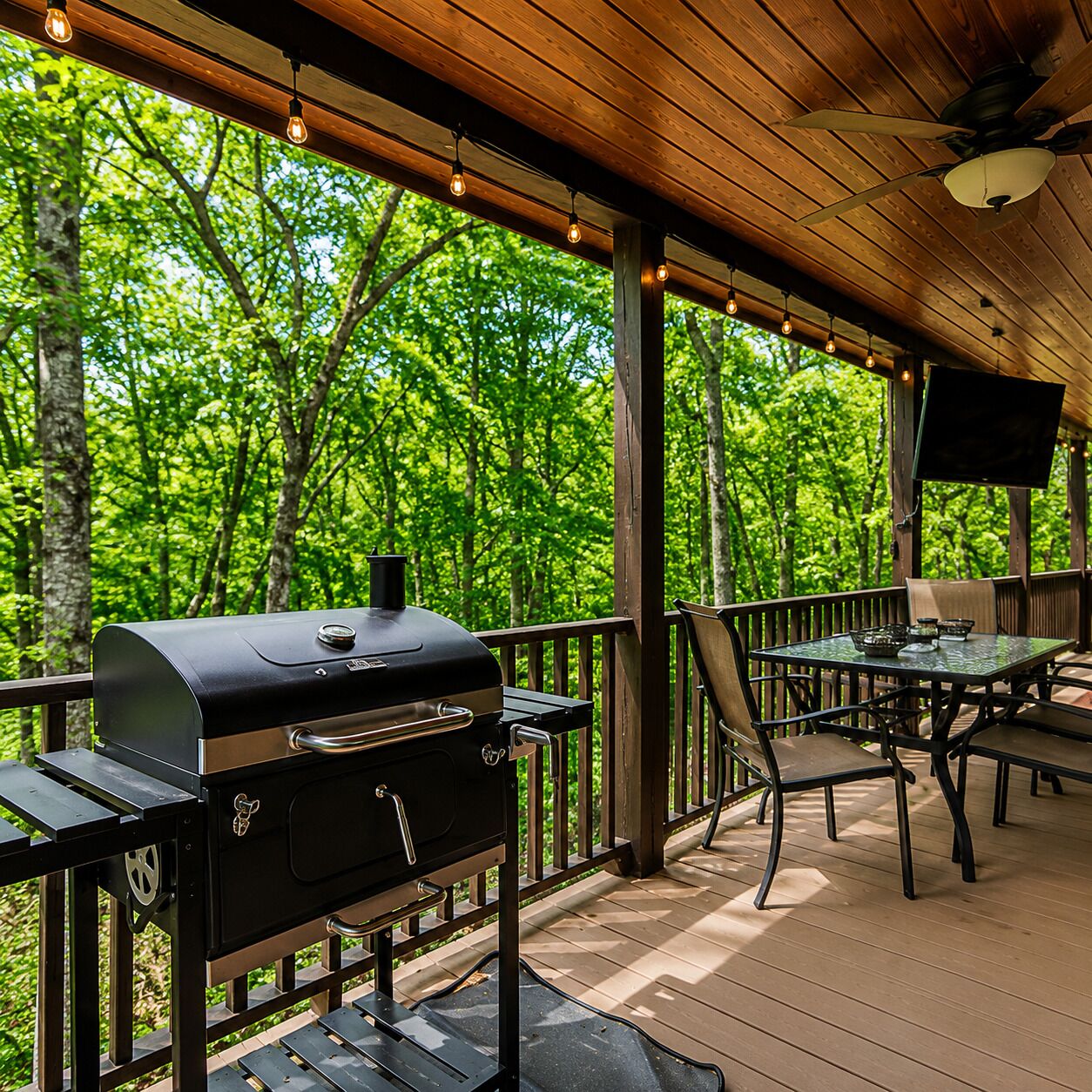 An outdoor deck with a barbecue grill, seating area, and a TV mounted on the wall.