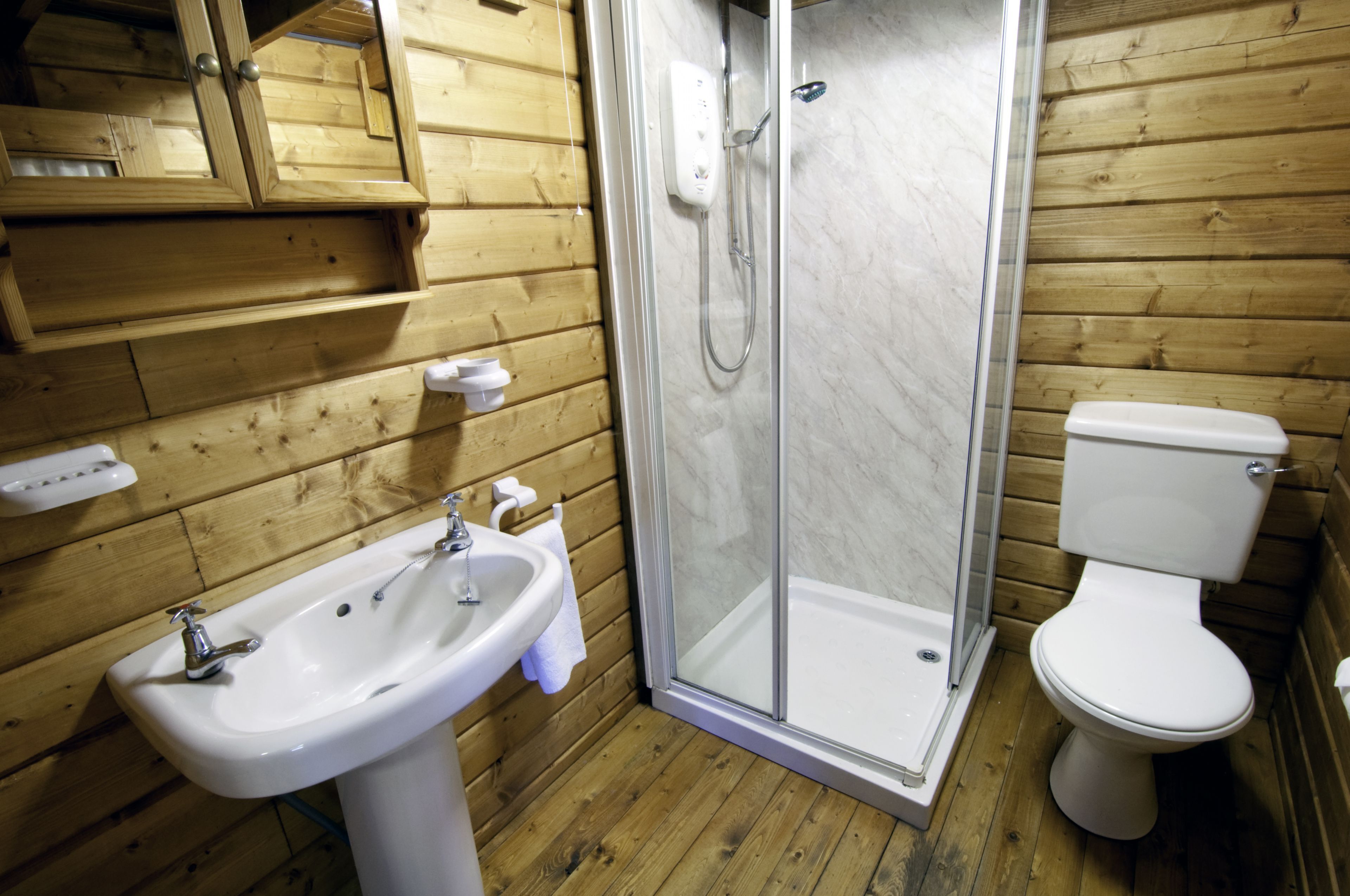 Baño de cabaña de madera con ducha envuelta en vidrio, lavamanos e inodoro.