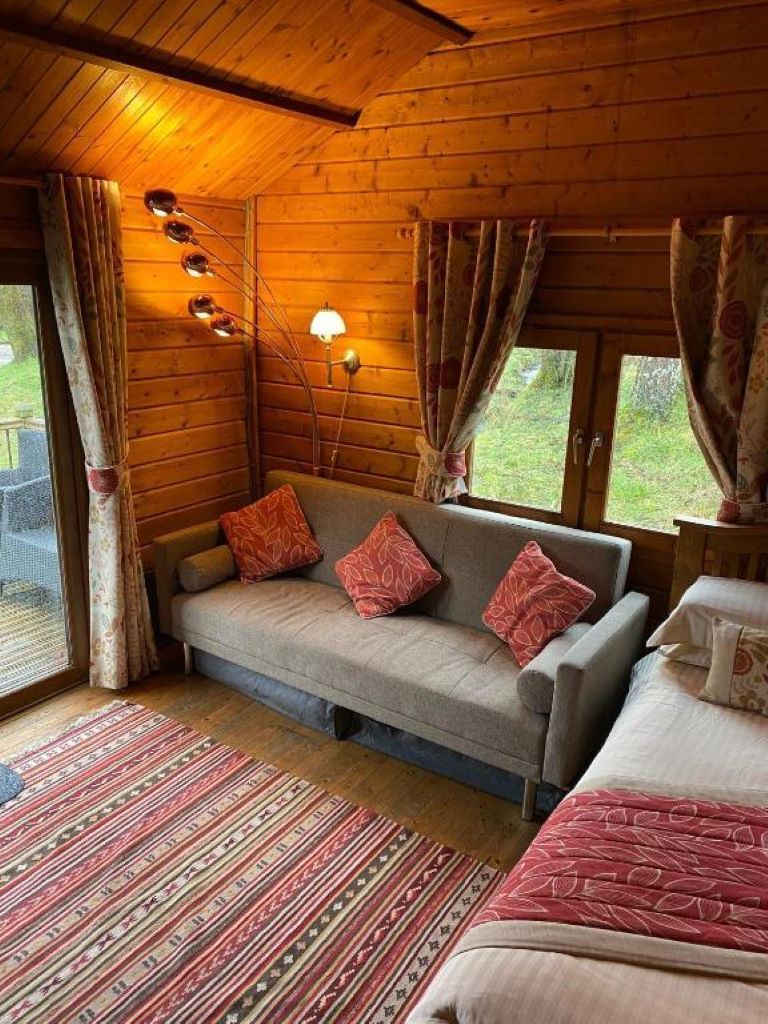 Una habitación tipo cabaña de madera con un sofá, una cama, un tapete estampado y una ventana con cortinas.