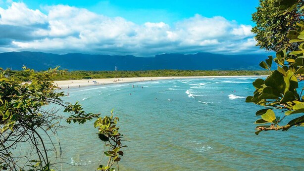 Una spiaggia con acque limpide, montagne in lontananza e un cielo nuvoloso.