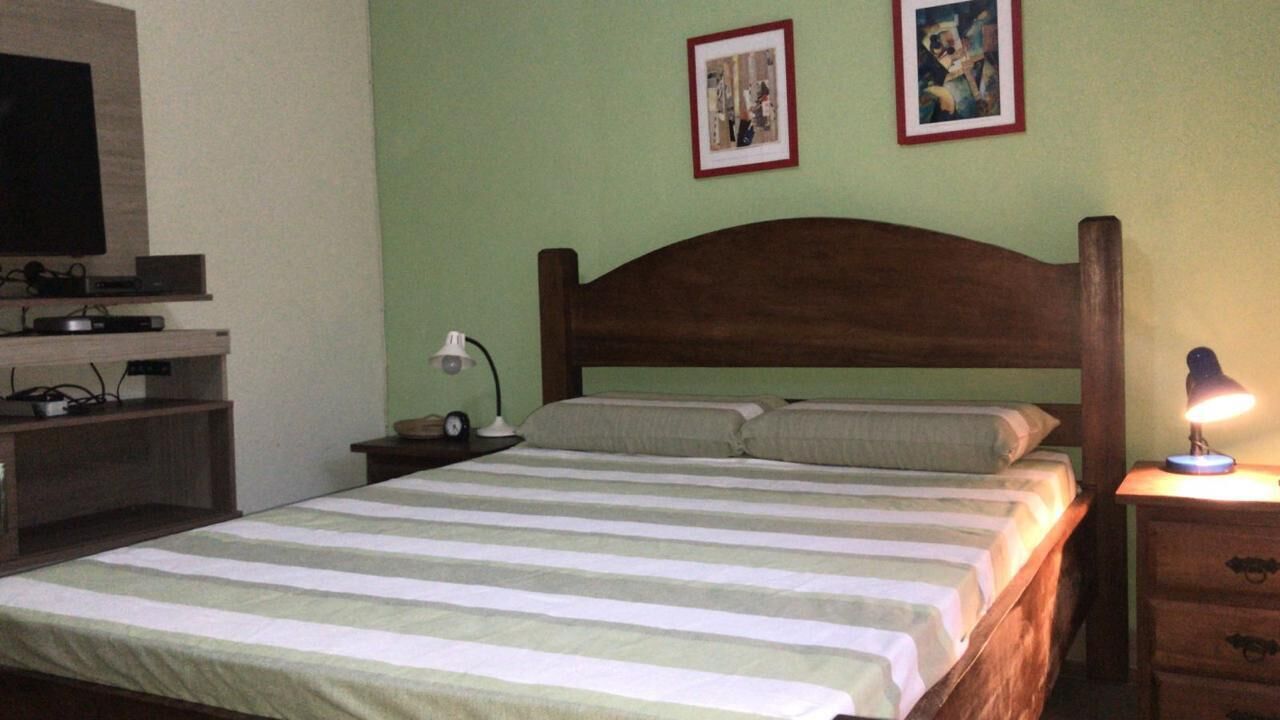 Una cama con cabecera de madera, una mesita de noche con lámpara y un televisor sobre un mueble.