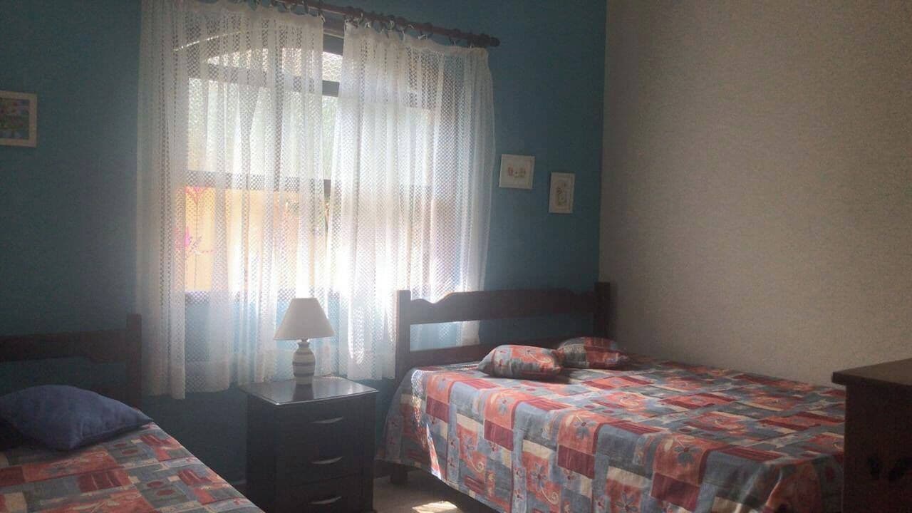 A bedroom with two beds, a nightstand, a lamp, and a window with sheer curtains.