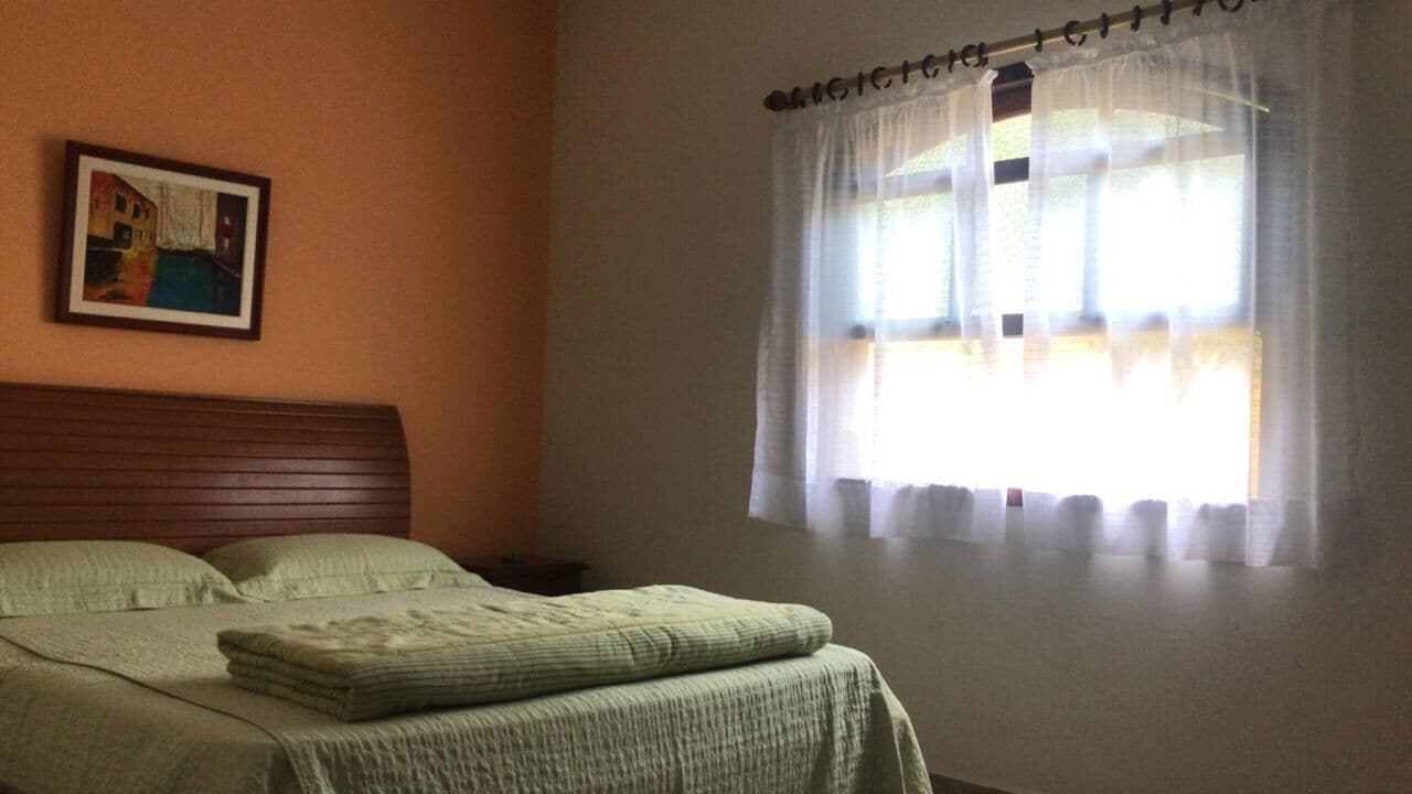 A bedroom with a bed, a nightstand, a framed picture on the wall, and a window with sheer curtains.