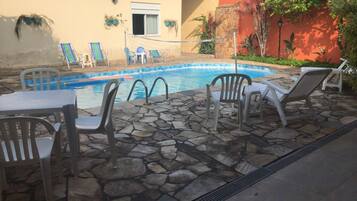 Uma área de piscina com piso de pedra, espreguiçadeiras e uma mesa.