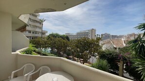 Varanda com mesa e cadeiras, vista para área residencial com árvores e edifícios.