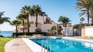 Una piscina con lettini, palme e un edificio con balconi.