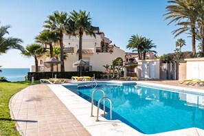 A swimming pool with lounge chairs, palm trees, and a building with balconies. - AS MDS 309 in Mijas Costa (Mijas)