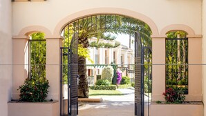 Un ingresso ad arco con un viale recintato che conduce a un edificio con un giardino curato e una palma.