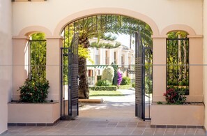 An arched entrance with a gated pathway leading to a building with a manicured garden and a palm tree. - AS MDS 309 in Mijas Costa (Mijas)
