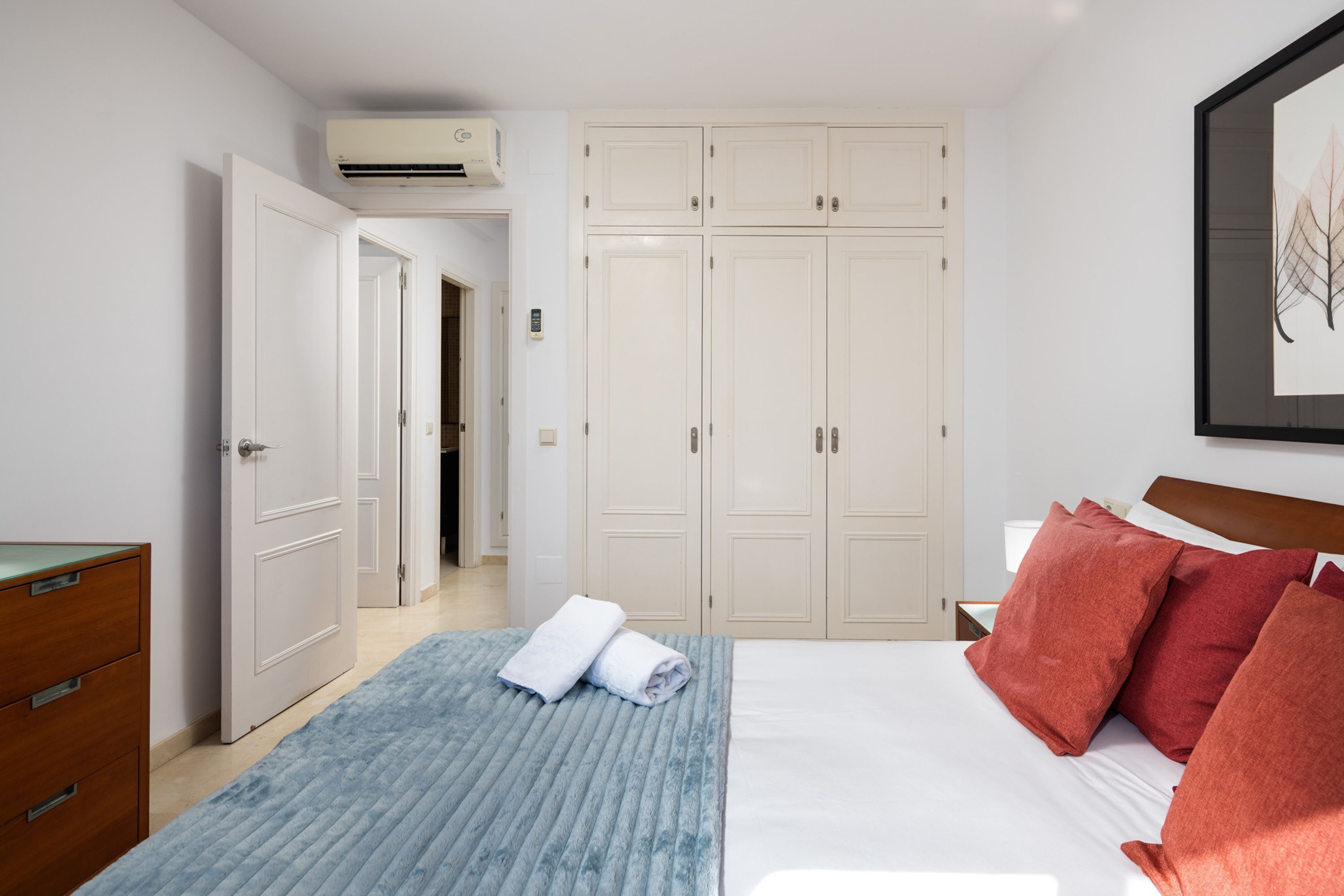 Een slaapkamer met een bed, een kledingkast, een dressoir en een lijst met een afbeelding aan de muur.