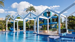 Una piscina con scivoli e zona coperta, circondata da palme e vegetazione.
