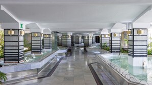 Una hall d'albergo con una fontana centrale, zone relax e illuminazione moderna.