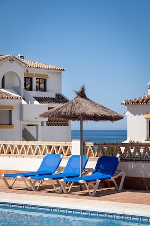 A pool area with blue lounge chairs and a thatched umbrella, overlooking the sea. - AS PM 27A in Mijas Costa (Mijas)