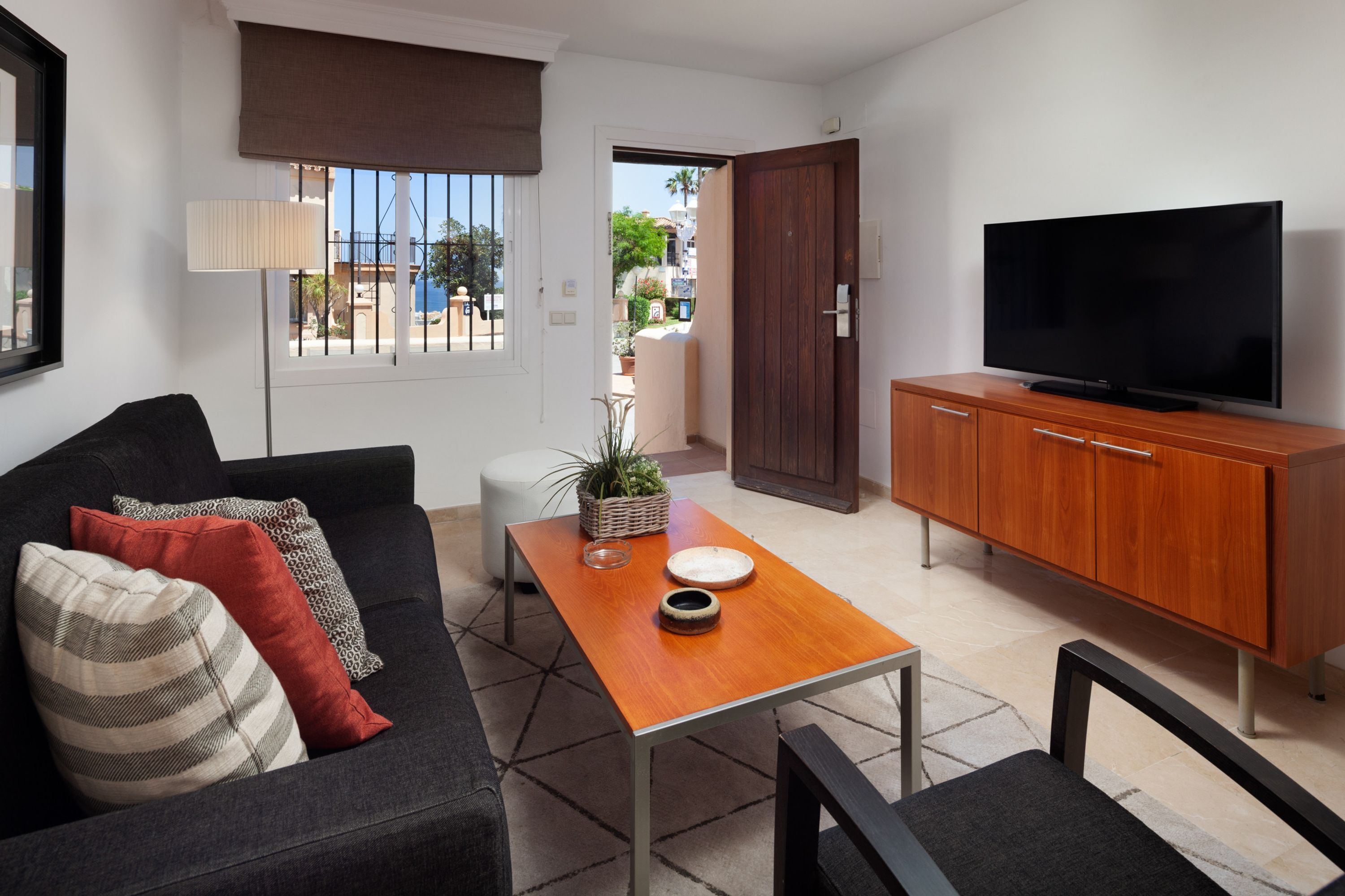 A living room with a sofa, a coffee table, a TV on a wooden cabinet, and a view through a door.