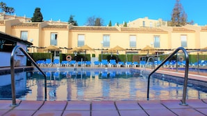En swimmingpool med blå stolar, en livboj och en byggnad med balkonger i bakgrunden.