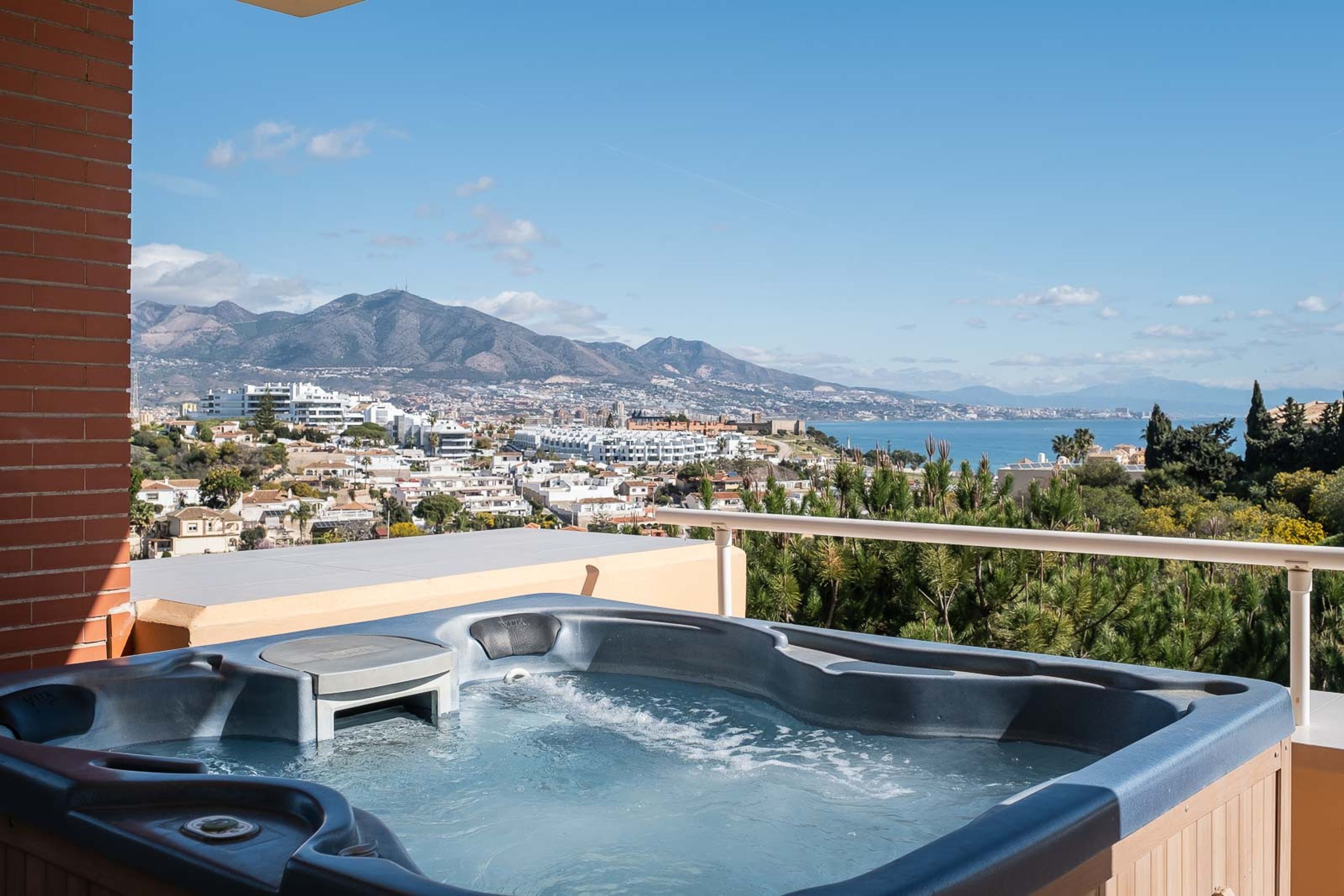 A hot tub on a balcony with a cityscape and mountains in the background.