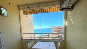 A balcony with a table and chairs, a view of the sea, and a building in the background. - Tamarindos 1002 in Benalm Dena (Benalmádena)