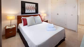 Una cama bien hecha con almohadas, una lámpara de noche, una obra de arte enmarcada sobre la cama y un armario al fondo.