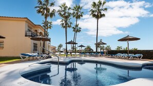 A swimming pool with lounge chairs and palm trees, surrounded by a building with balconies. - AS MD 3C3 in Mijas Costa (Mijas)