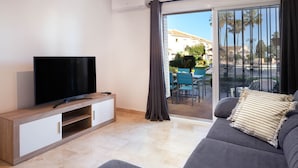 A modern living room with a flat-screen TV, a sofa, and a sliding glass door leading to an outdoor patio. - AS MDS 159 in Mijas Costa (Mijas)