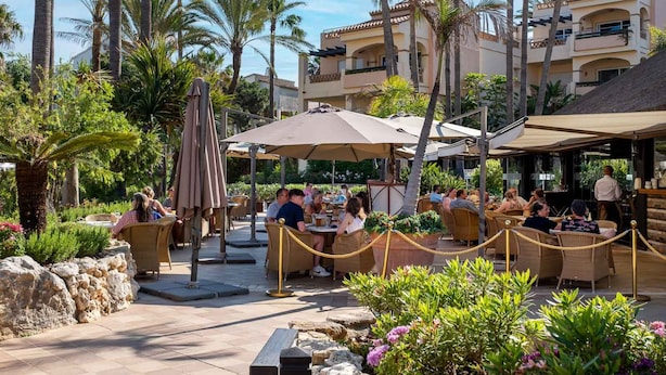An outdoor dining area with tables and chairs, surrounded by palm trees and a building with balconies. - AS MDS 159 in Mijas Costa (Mijas)