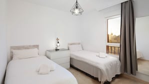 A bedroom with two beds, a nightstand, a lamp, a window with curtains, and a hanging light fixture. - AS MDS 159 in Mijas Costa (Mijas)