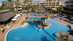 Un complexe hôtelier doté d’une grande piscine, de chaises longues, de palmiers et d’un bâtiment avec des balcons.