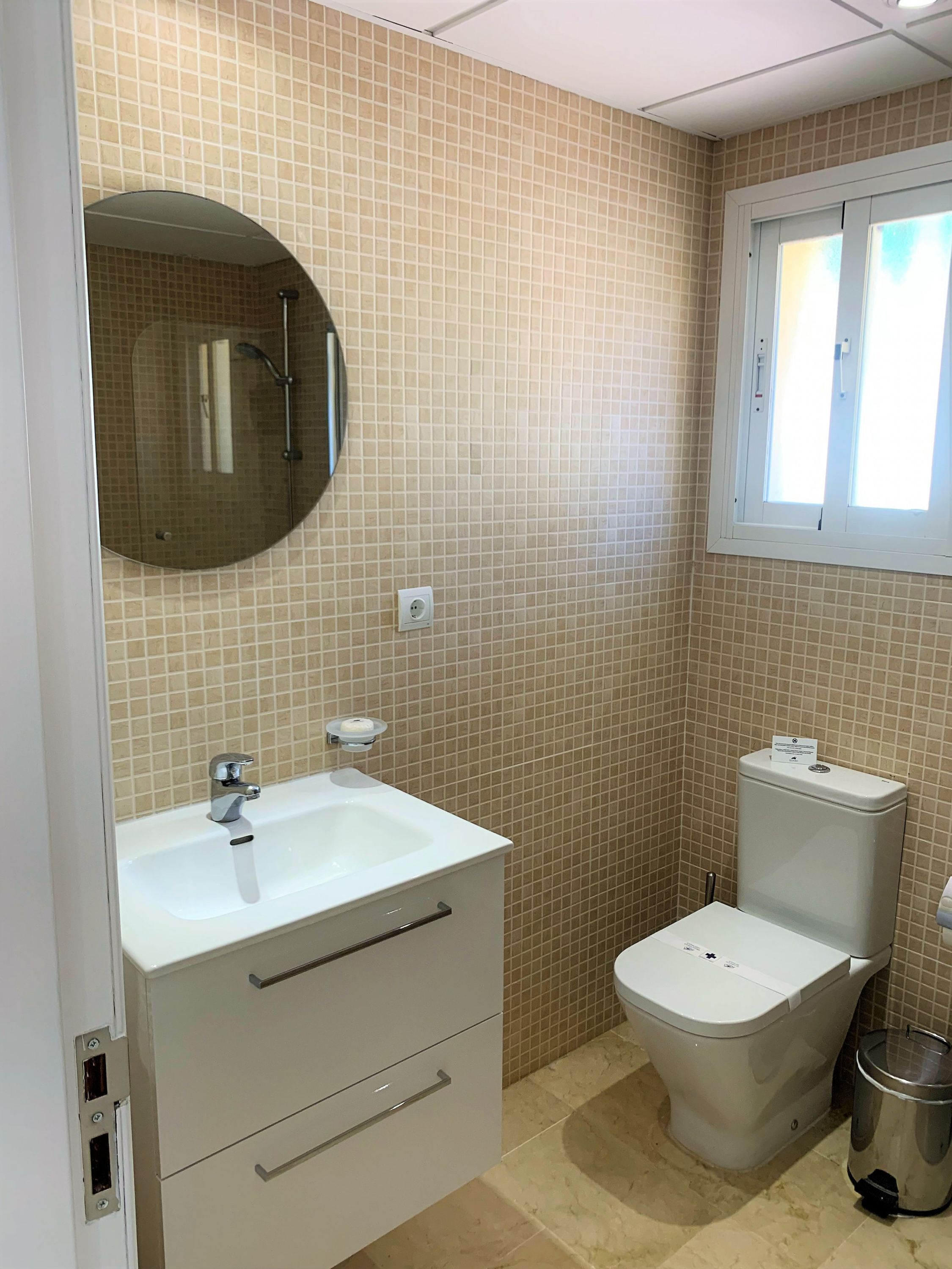 A bathroom with a sink, mirror, toilet, and trash bin.