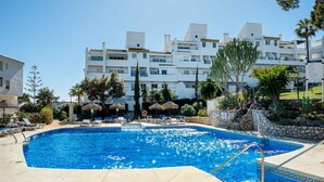 Una piscina con sillas de descanso y sombrillas, rodeada de edificios y palmeras.