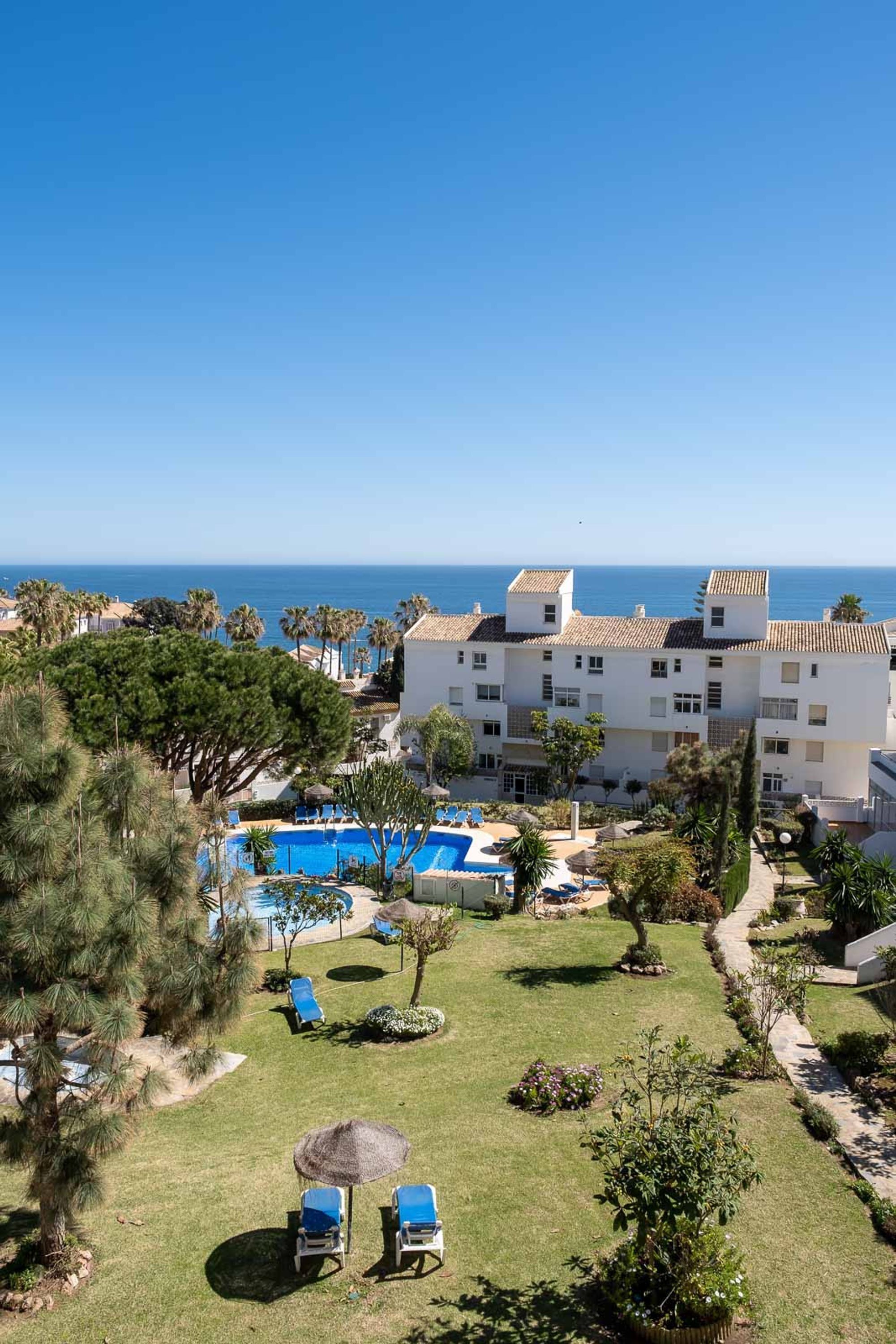 Un complexe hôtelier doté d’une piscine, de chaises longues et offrant une vue sur la mer.