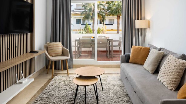 A modern living room with a flat-screen TV, a sofa, a chair, a small table, and a view of a balcony with outdoor furniture. - AS EXT Calanova 71A in Mijas Costa (Mijas)