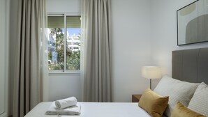 Una camera d'albergo con un letto, un comodino, una lampada e una finestra con tende.