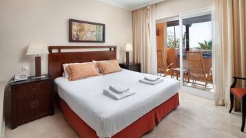 A hotel room with a large bed, two bedside tables, a painting, and a balcony with chairs.