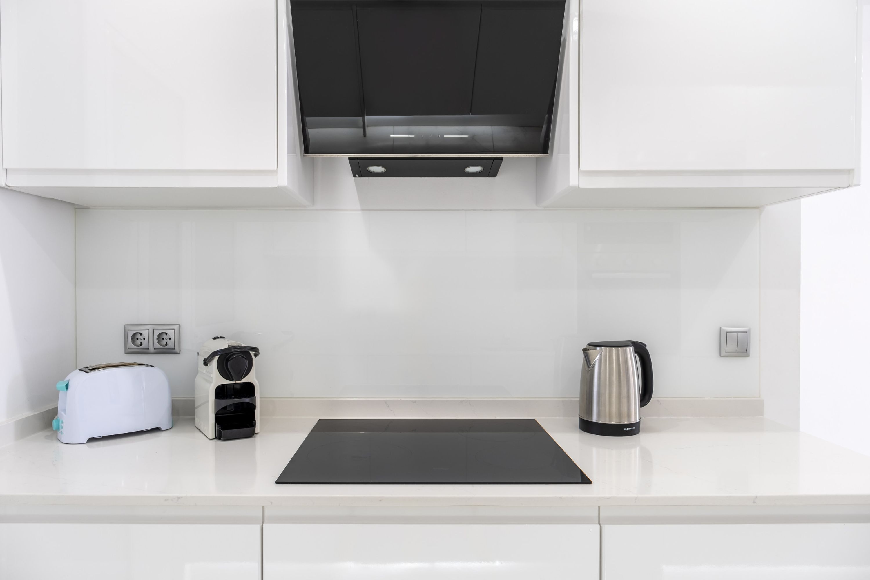 A modern kitchen with white cabinets, a black countertop, a toaster, a coffee maker, and a kettle.