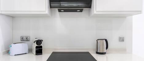 A modern kitchen with white cabinets, a black countertop, a toaster, a coffee maker, and a kettle.
