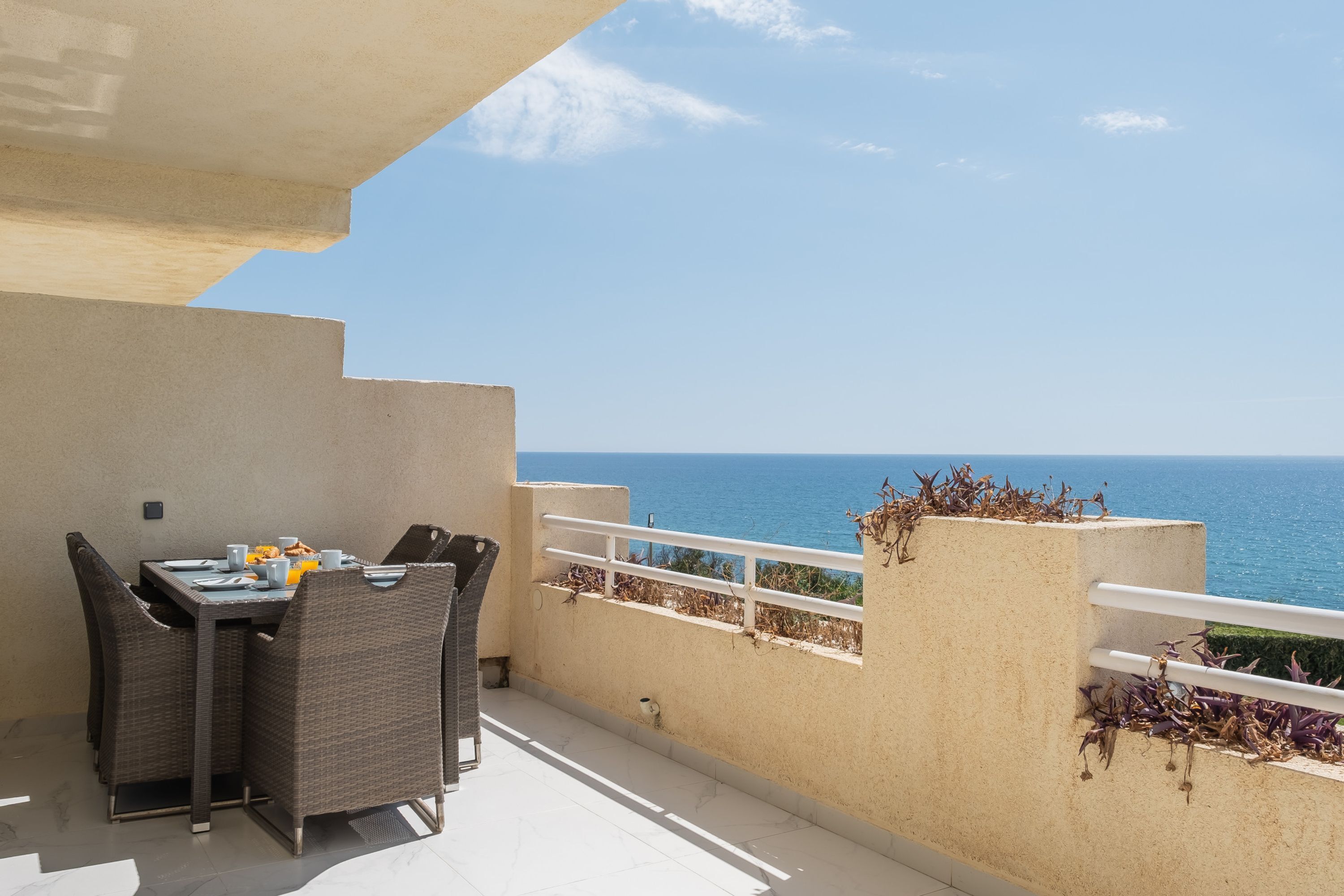A balcony with a table and chairs, a railing, and a view of the sea.