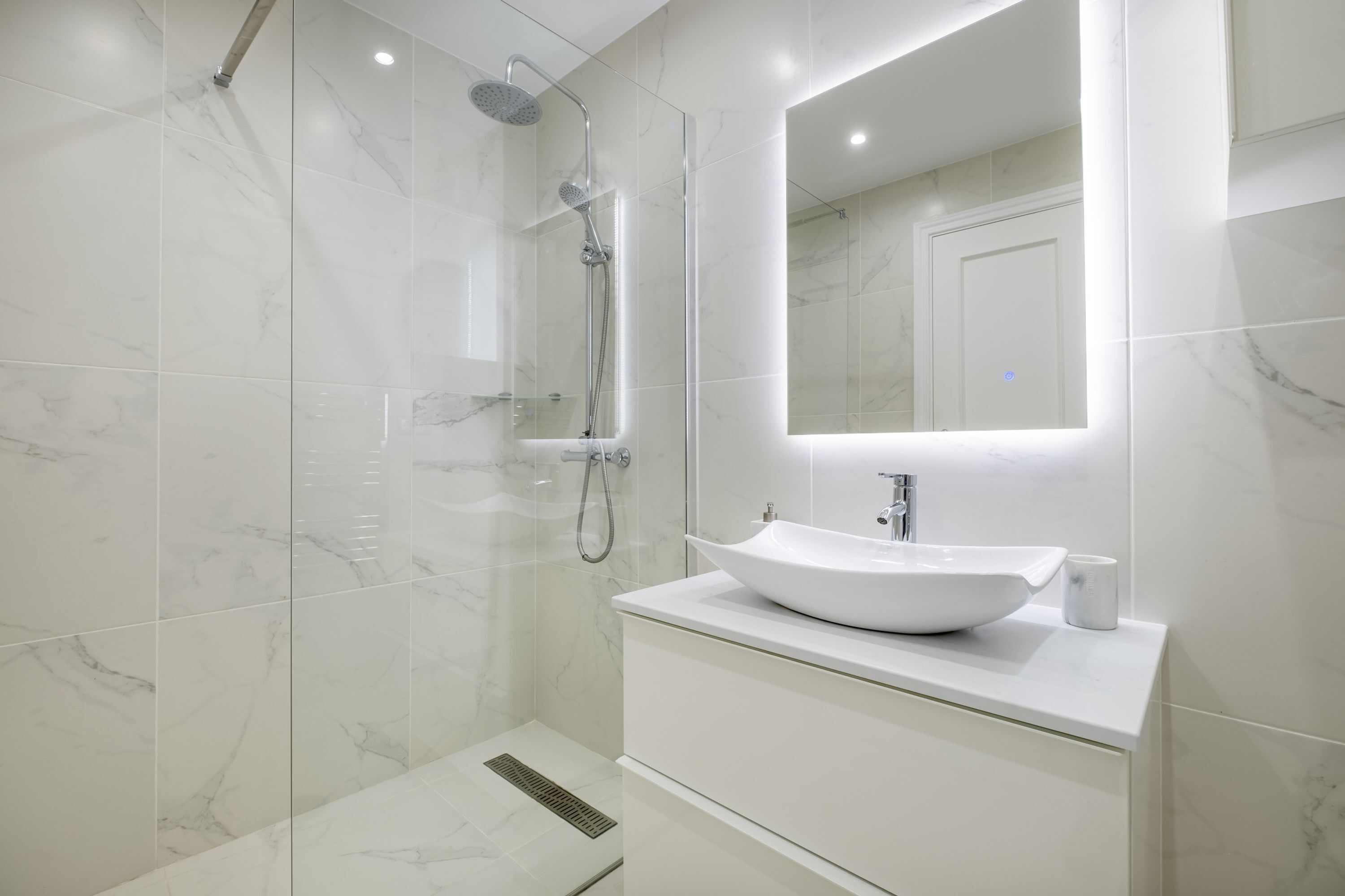 Une salle de bain moderne avec une douche à parois de verre, un lavabo blanc et un grand miroir.