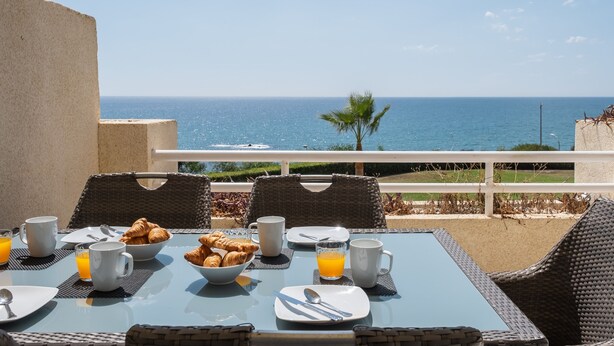 Ein Frühstückstisch mit Croissants, Orangensaft und Kaffee, mit Blick auf die Küste.
