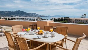 A dining table with wicker chairs, plates, cups, and a teapot on a terrace with a view of a city and mountains. - AS MM C10 in Mijas Costa (Mijas)