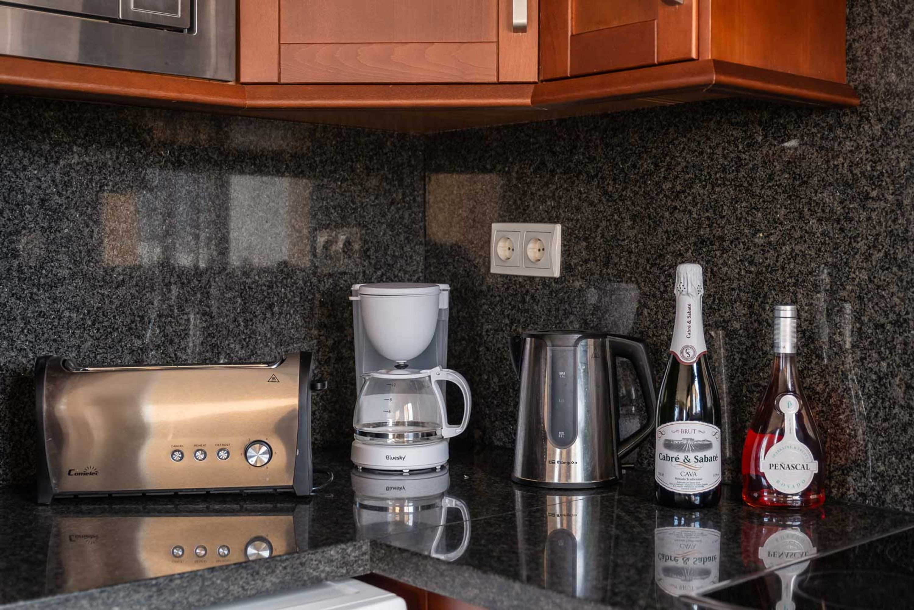A kitchen counter with a coffee maker, a kettle, and two bottles of wine.