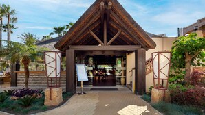 A building entrance with a thatched roof, palm trees, and a paved walkway. - AS LJ D 3 A in Mijas Costa (Mijas)