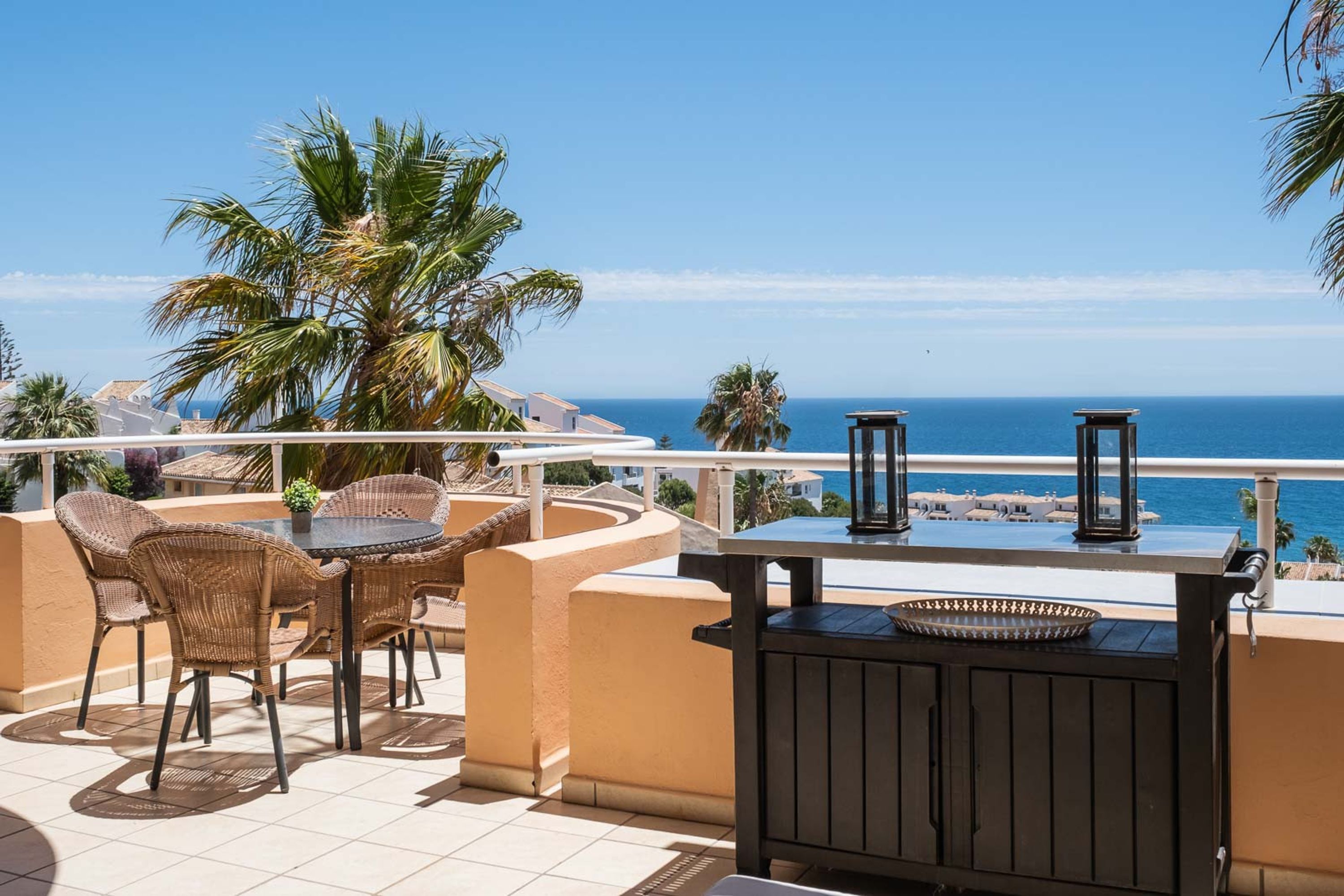 Een terras met rieten meubilair, een barbecue en uitzicht op zee.